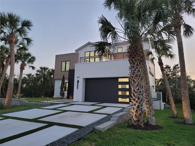 807 N Flagler Ave, Flagler Beach, FL 32136 - modern home featuring concrete driveway, stucco siding, a balcony, an attached garage, and a front lawn
