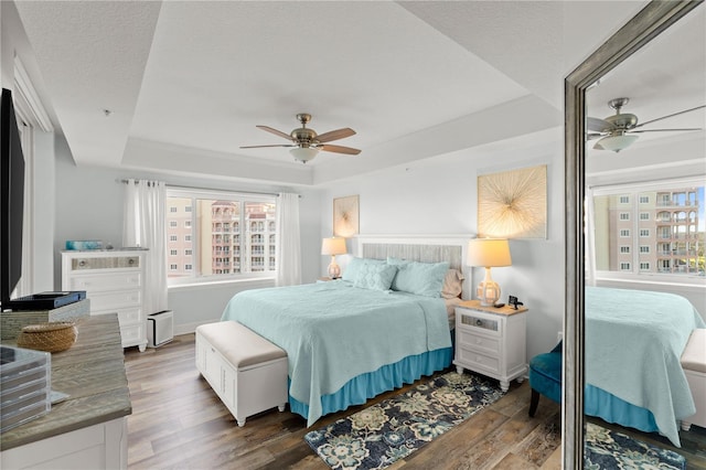 bedroom with a tray ceiling, wood finished floors, and ceiling fan