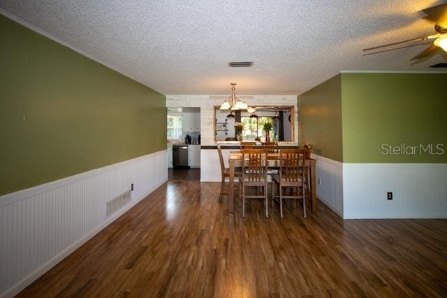 dining room featuring a wainscoted wall, a textured ceiling, a chandelier, wood finished floors, and a ceiling fan
