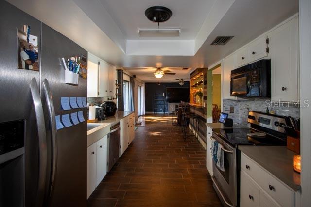 kitchen featuring appliances with stainless steel finishes, backsplash, white cabinetry, and a raised ceiling