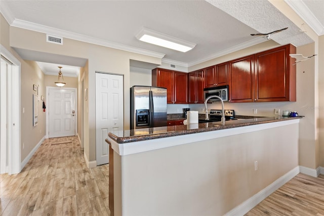 kitchen with stainless steel appliances, a peninsula, light wood-style floors, reddish brown cabinets, and ornamental molding