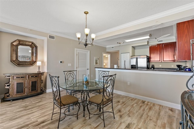 dining room featuring light wood-style floors, ornamental molding, a textured ceiling, a chandelier, and baseboards