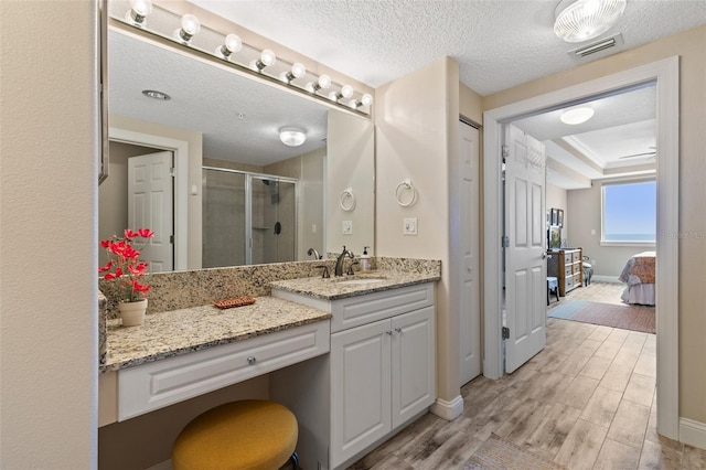 full bath featuring a stall shower, vanity, baseboards, a textured ceiling, and wood finished floors