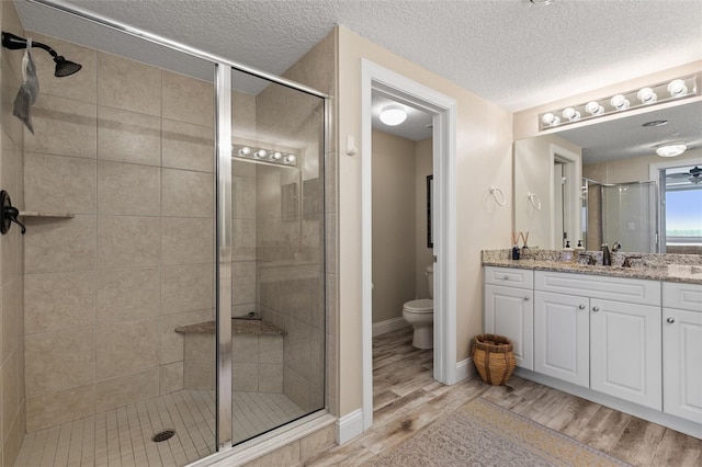full bath featuring a shower stall, toilet, wood finished floors, a textured ceiling, and baseboards
