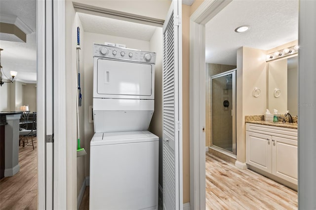 laundry room with stacked washing machine and dryer, a textured ceiling, light wood-style flooring, and baseboards