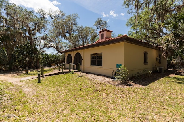 back of house with a lawn, stucco siding, central AC, and a tile roof