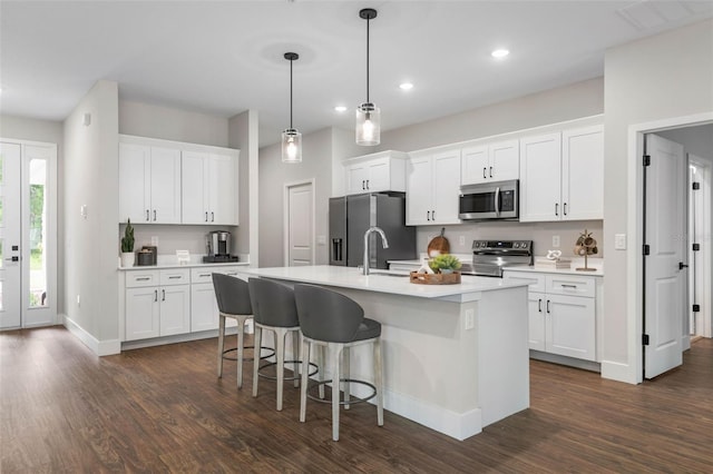 kitchen with appliances with stainless steel finishes, dark wood finished floors, a center island with sink, light countertops, and recessed lighting