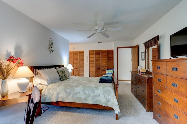 bedroom featuring two closets, light carpet, and ceiling fan