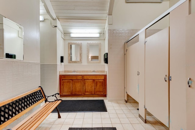 full bath featuring tile walls, tile patterned flooring, double vanity, and a wainscoted wall