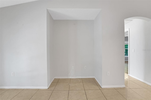 empty room featuring arched walkways, light tile patterned floors, and baseboards