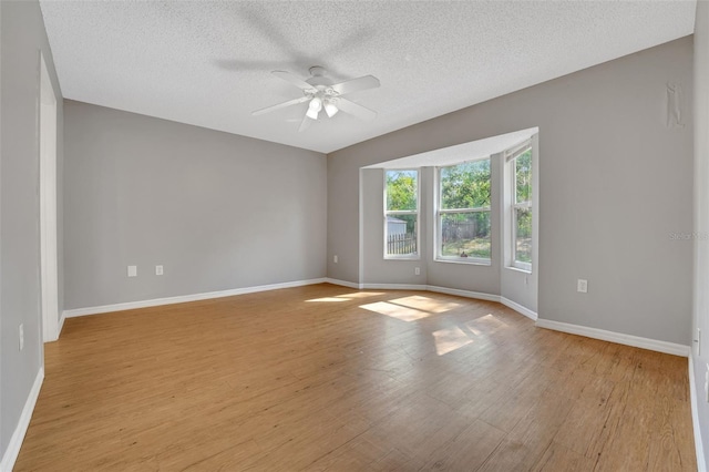 spare room featuring ceiling fan, light wood-style flooring, baseboards, and a textured ceiling
