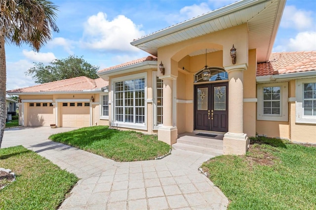view of exterior entry featuring a tile roof, stucco siding, an attached garage, and driveway