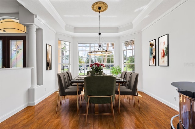 dining space with wood finished floors, ornate columns, a raised ceiling, baseboards, and healthy amount of natural light