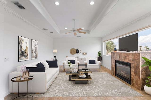 living room with recessed lighting, a ceiling fan, a tiled fireplace, ornamental molding, and a tray ceiling