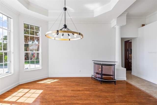 unfurnished dining area with crown molding, plenty of natural light, a chandelier, a raised ceiling, and wood finished floors