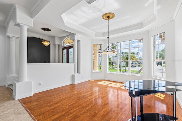 dining area featuring decorative columns, a chandelier, a raised ceiling, and ornamental molding
