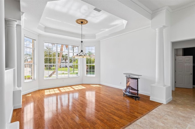 unfurnished dining area with ornate columns, crown molding, baseboards, a chandelier, and a tray ceiling