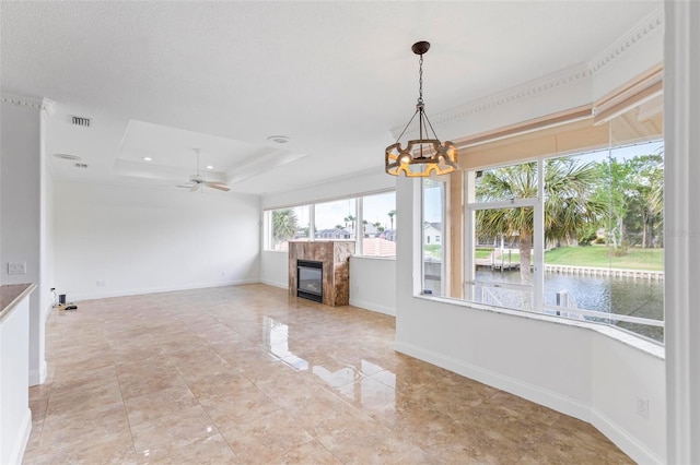 unfurnished living room featuring a water view, a chandelier, a tray ceiling, a glass covered fireplace, and baseboards