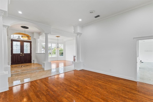entryway featuring decorative columns, wood finished floors, a chandelier, baseboards, and ornamental molding