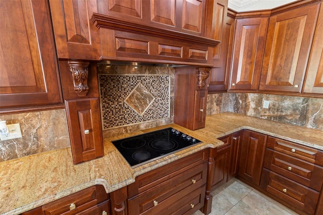 kitchen with black electric cooktop, backsplash, light stone countertops, light tile patterned floors, and brown cabinetry