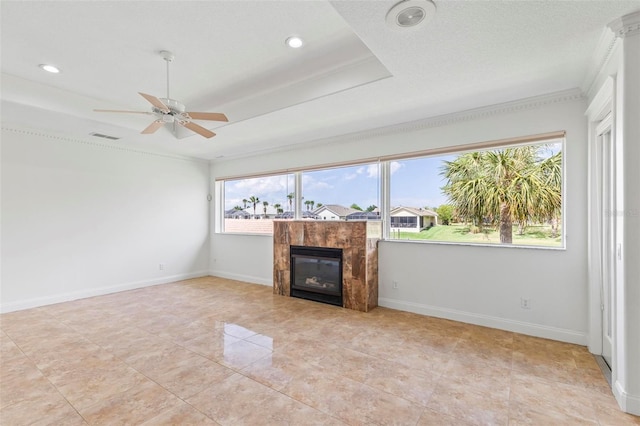 unfurnished living room with a ceiling fan, a tray ceiling, a tile fireplace, recessed lighting, and ornamental molding