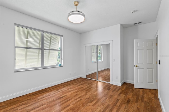 unfurnished bedroom with wood finished floors, baseboards, and a closet