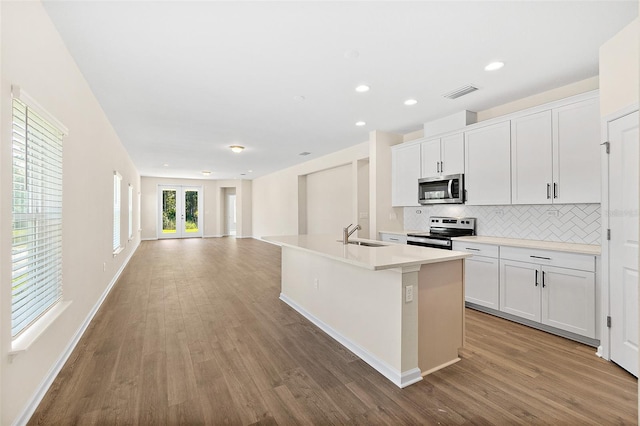 137 Nighthawk Ln, Palm Coast, FL 32164 - kitchen with appliances with stainless steel finishes, a sink, tasteful backsplash, wood finished floors, and a center island with sink
