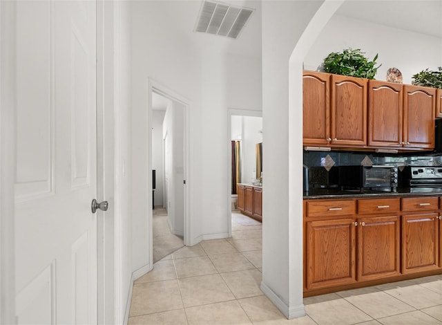 91 Breeze Hill Ln, Palm Coast, FL 32137 - kitchen with arched walkways, light tile patterned floors, brown cabinetry, a towering ceiling, and decorative backsplash