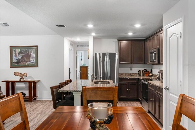 9 Waldron Pl, Palm Coast, FL 32164 - kitchen with appliances with stainless steel finishes, light wood-style flooring, light stone countertops, dark brown cabinetry, and a kitchen island with sink