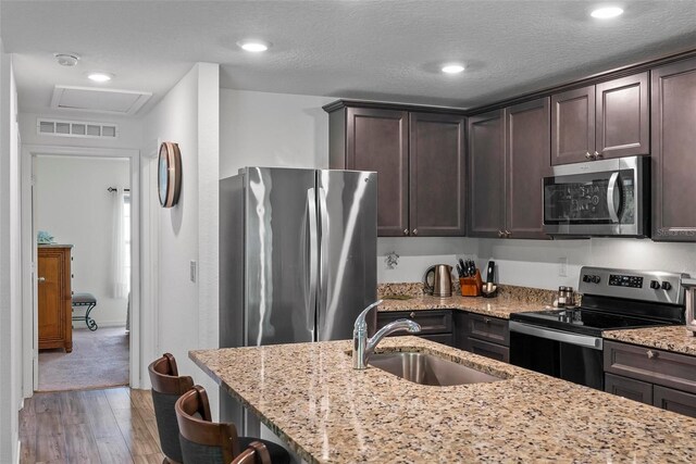 9 Waldron Pl, Palm Coast, FL 32164 - kitchen featuring stainless steel appliances, a sink, dark brown cabinets, light wood-style flooring, and light stone countertops