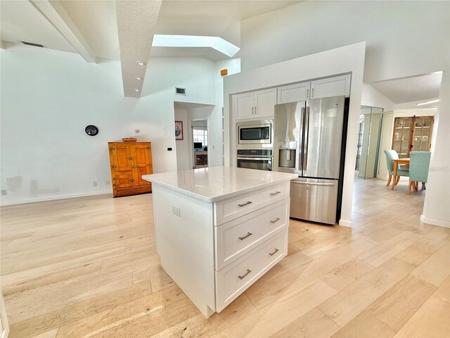 4 Cotton Ct, Palm Coast, FL 32137 - kitchen with stainless steel appliances, a skylight, light stone counters, light wood-type flooring, and a high ceiling