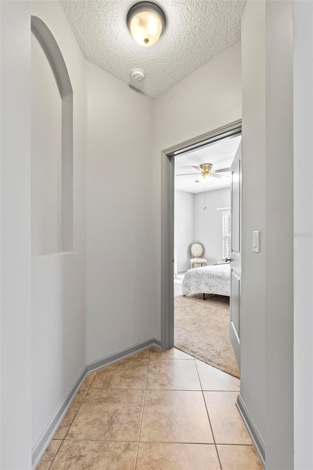 123 N Starling Dr, Palm Coast, FL 32164 - hall with a textured ceiling, light tile patterned floors, baseboards, arched walkways, and light colored carpet