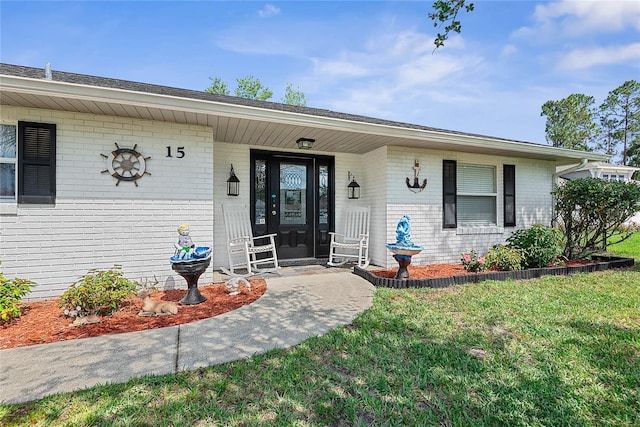 property entrance featuring brick siding, a porch, and a yard