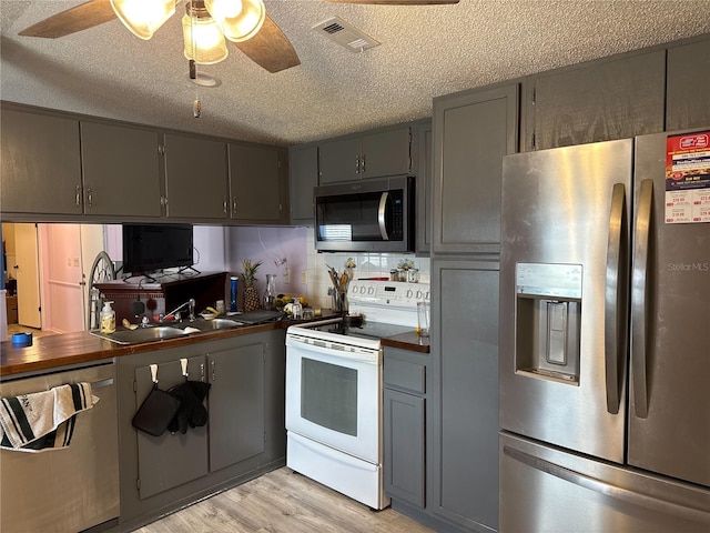 kitchen with stainless steel appliances, gray cabinets, a sink, dark countertops, and a textured ceiling