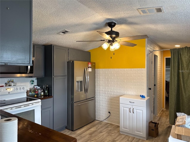 kitchen featuring stainless steel appliances, a textured ceiling, light wood-style flooring, and a ceiling fan