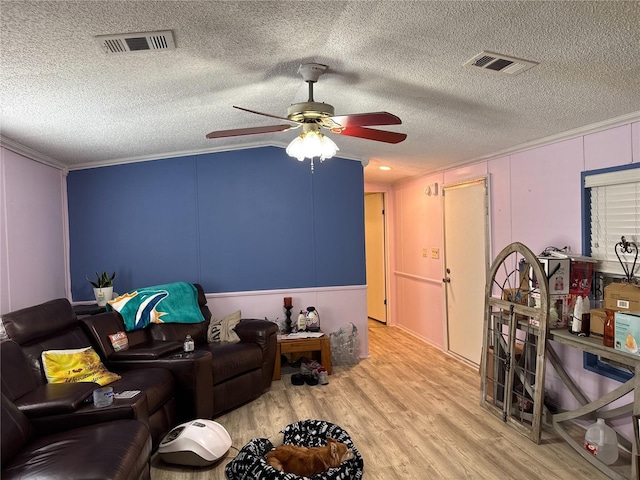 living room with ceiling fan, wood finished floors, a textured ceiling, a decorative wall, and ornamental molding