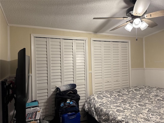 bedroom featuring multiple closets, a textured ceiling, ornamental molding, and ceiling fan