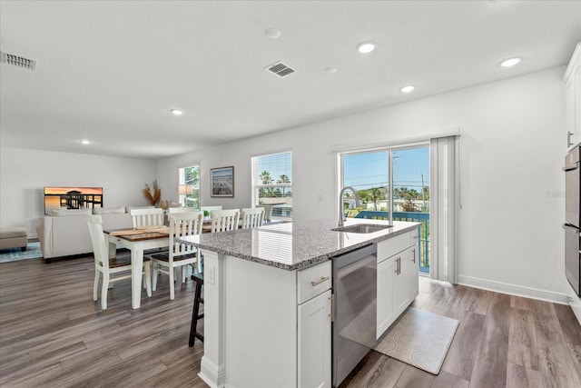 3828 S Atlantic Ave, Daytona Beach, FL 32118 - kitchen with dishwasher, wood finished floors, an island with sink, light stone counters, and white cabinetry