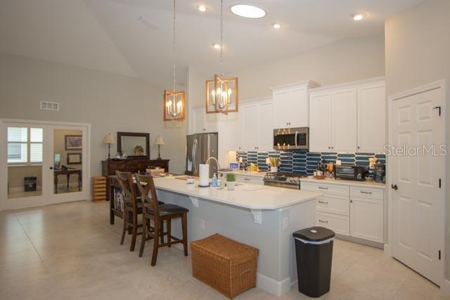 37 Lagoon Way, Palm Coast, FL 32137 - kitchen with appliances with stainless steel finishes, backsplash, a breakfast bar area, an island with sink, and a chandelier