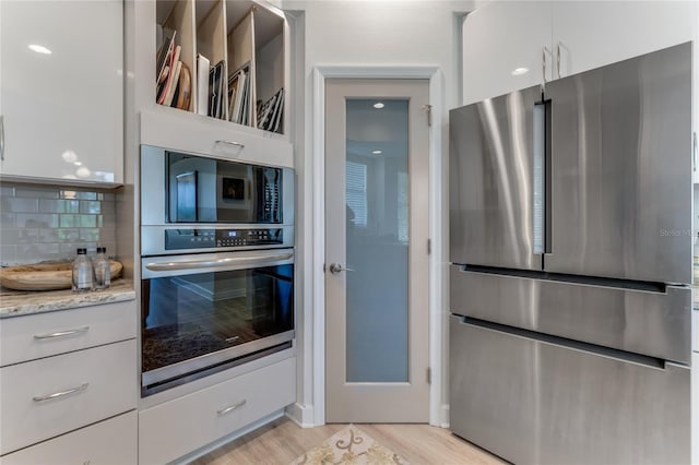 200 Riverfront Dr Unit B204, Palm Coast, FL 32137 - kitchen with appliances with stainless steel finishes, backsplash, light stone countertops, white cabinets, and light wood-type flooring