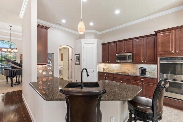 716 Woodbridge Ct, Ormond Beach, FL 32174 - kitchen featuring appliances with stainless steel finishes, washer / clothes dryer, a sink, a chandelier, and arched walkways