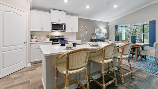 151 Greenwood Dr, Palm Coast, FL 32137 - kitchen with stainless steel appliances, light countertops, vaulted ceiling, a center island with sink, and crown molding