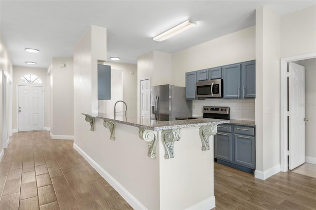 kitchen featuring stainless steel appliances, a breakfast bar, light wood-style floors, a peninsula, and light stone counters
