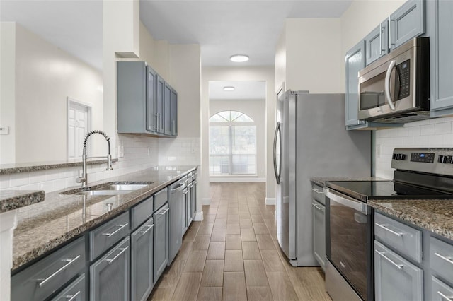 kitchen with stainless steel appliances, a sink, dark stone counters, and decorative backsplash