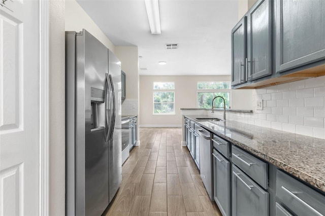 kitchen featuring a sink, stainless steel appliances, gray cabinets, light wood finished floors, and tasteful backsplash