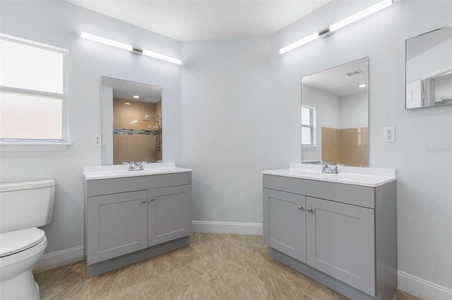 bathroom featuring a shower stall, toilet, baseboards, and two vanities