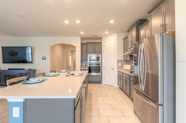 2840 Monaghan Dr, Ormond Beach, FL 32174 - kitchen with appliances with stainless steel finishes, a sink, arched walkways, gray cabinetry, and under cabinet range hood