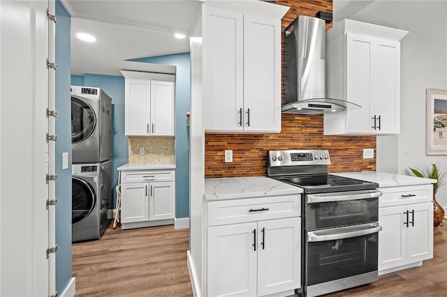 54 Fordham Ln, Palm Coast, FL 32137 - kitchen with range with two ovens, stacked washer / dryer, wall chimney exhaust hood, light wood-type flooring, and white cabinets