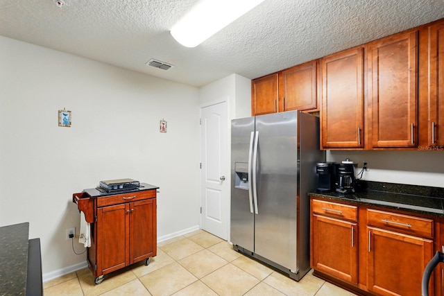 kitchen with stainless steel fridge, light tile patterned floors, a textured ceiling, dark stone countertops, and baseboards
