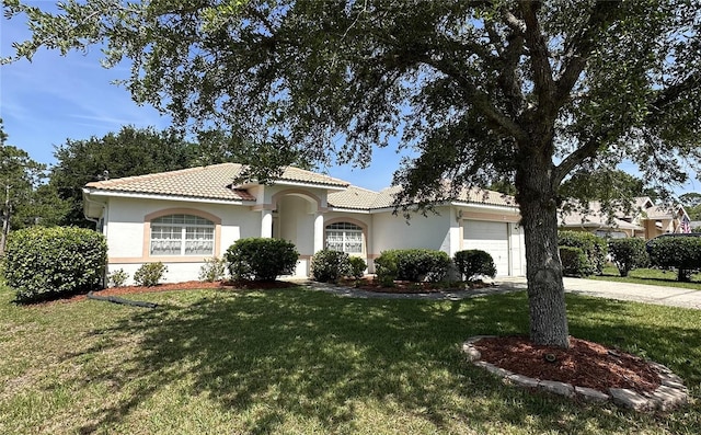 mediterranean / spanish home with an attached garage, a tile roof, a front lawn, stucco siding, and driveway